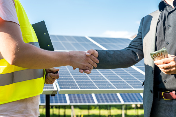 Dwie osoby ściskające dłonie przed panelem słonecznym po zawarciu umowy w sprawie energii odnawialnej   - Zdjęcie, obraz