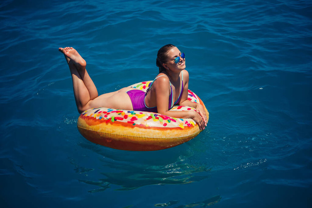 Hermosa joven feliz en un traje de baño con un anillo inflable relajante en el mar azul. Día soleado, vacaciones junto al mar, turismo - Foto, Imagen