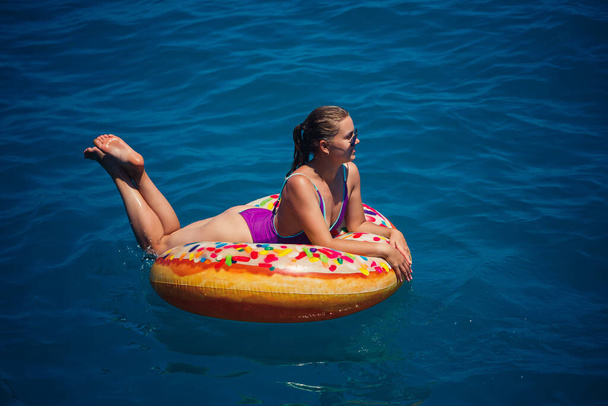 Mooie gelukkige jonge vrouw in een zwempak met een opblaasbare ring ontspannen in de blauwe zee. Zonnige dag, vakantie aan zee, toerisme - Foto, afbeelding