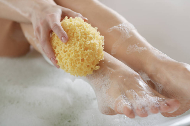 Γυναίκα τρίβει το πόδι της με σφουγγάρι ενώ κάνει μπάνιο, κοντινό πλάνο - Φωτογραφία, εικόνα