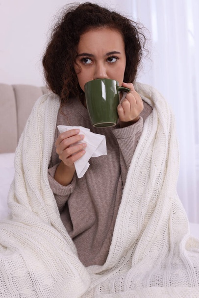 Sick African American woman with tissue and cup of drink in bed at home - Foto, Bild