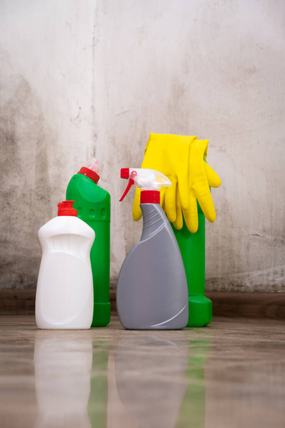 Κοντινό πλάνο των προϊόντων καθαρισμού στέκεται στο πάτωμα, κίτρινα γάντια για την αφαίρεση μούχλα από τους τοίχους. Έννοια του καθαρισμού, δουλειές του σπιτιού. Κάθετη φωτογραφία - Φωτογραφία, εικόνα