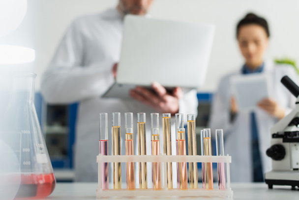selective focus of test tubes near scientists with gadgets on blurred background - Photo, Image