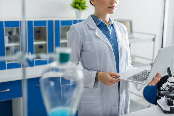 cropped view of scientist holding laptop in laboratory on blurred foreground - Fotó, kép