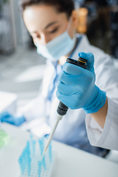 geneticista turvo em máscara médica trabalhando com micropipeta em laboratório - Foto, Imagem
