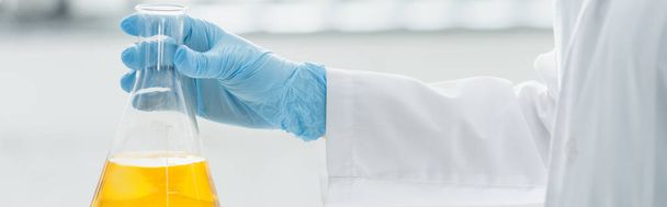 vista parziale dello scienziato in guanto di lattice con in mano fiaschetta medica con liquido giallo, banner - Foto, immagini