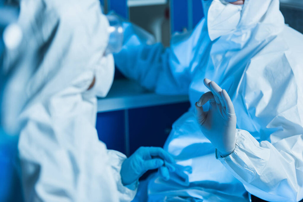Ausgeschnittene Ansicht eines Virologen im Warnanzug und Latexhandschuhen, der eine gute Geste neben dem Kollegen zeigt - Foto, Bild