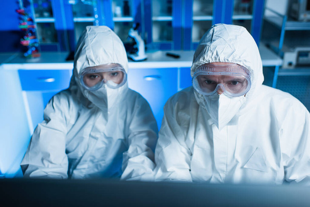 cientistas em fatos de proteção contra riscos, óculos de proteção e máscaras médicas que trabalham em laboratório - Foto, Imagem