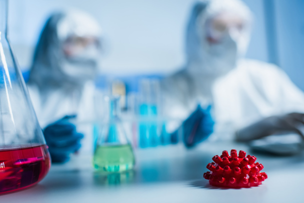 επιλεκτική εστίαση της φιάλης με κόκκινο υγρό και μοντέλο βακτηρίων του κορωναϊού κοντά σε θολή ιολόγους - Φωτογραφία, εικόνα