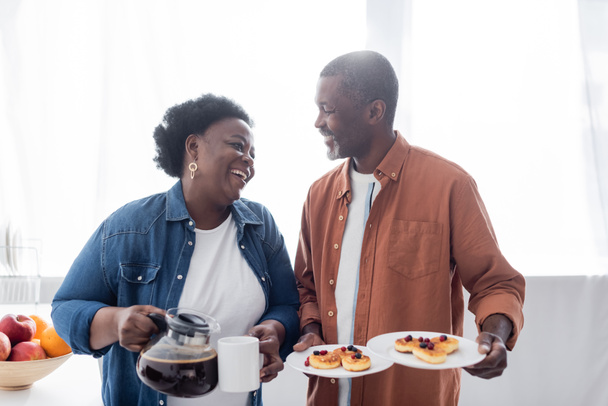 щасливий афроамериканський чоловік тримає тарілки з млинцями біля дружини
 - Фото, зображення