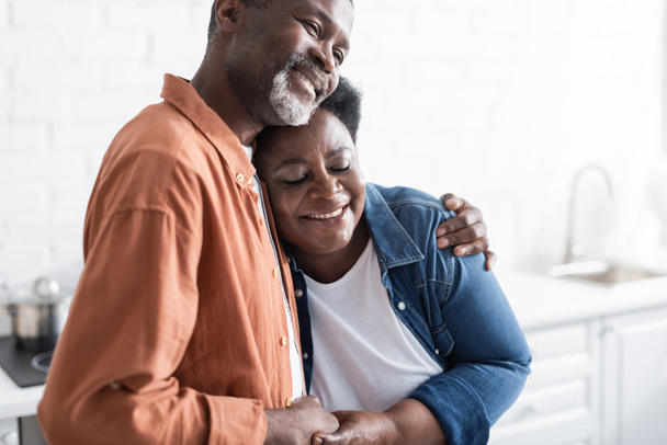 heureux et senior couple afro-américain tenant la main et étreignant à la maison - Photo, image
