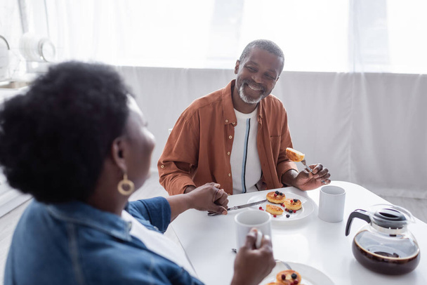 joyeux et senior couple afro-américain tenant la main tout en prenant le petit déjeuner  - Photo, image
