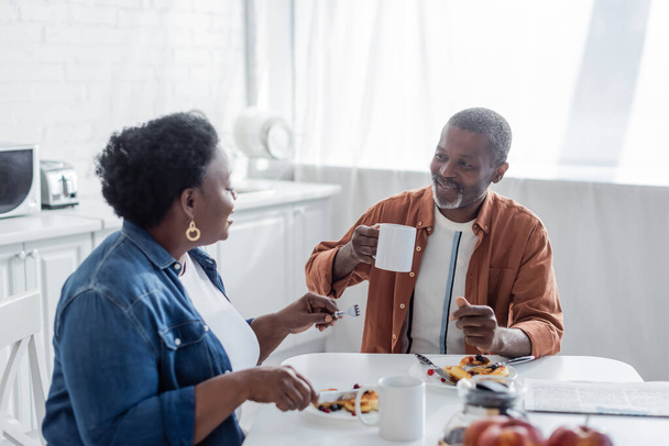 souriant homme afro-américain parler avec la femme aînée pendant le petit déjeuner  - Photo, image