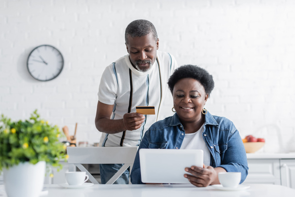 senior african american man holding credit card while online shopping with happy wife  - Photo, image