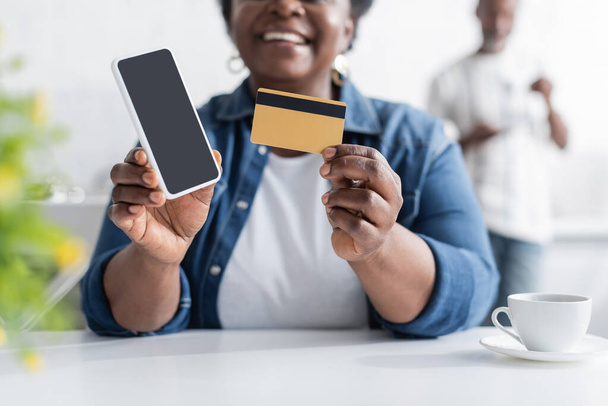vista cortada de mulher americana africana sênior feliz segurando cartão de crédito e smartphone com tela em branco  - Foto, Imagem