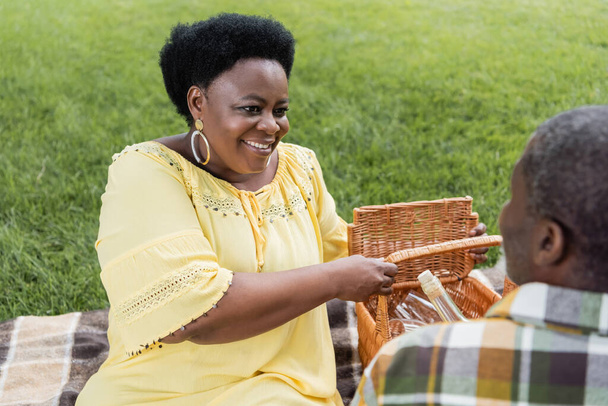 feliz africano americano mujer sonriendo cerca marido durante picnic  - Foto, Imagen