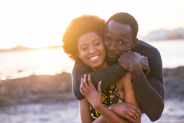 Cheerful black people couple hug and enjoy love and friendship together at the beach with sunset light in background. Concept of young adult's relationship in summer holiday vacation outdoor leisure - Фото, изображение
