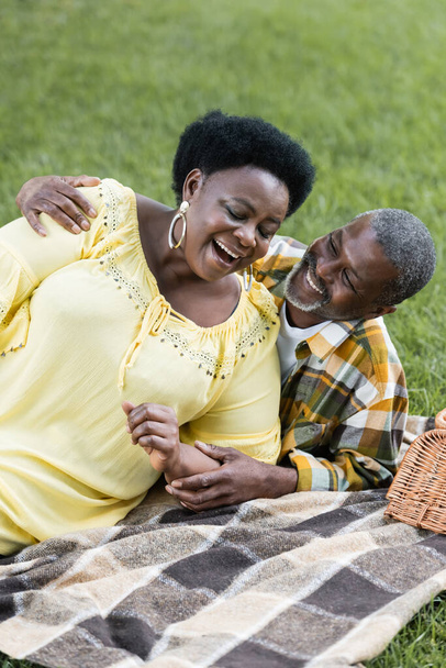 glimlachen en senior afrikaanse paar liggend op deken tijdens de picknick  - Foto, afbeelding