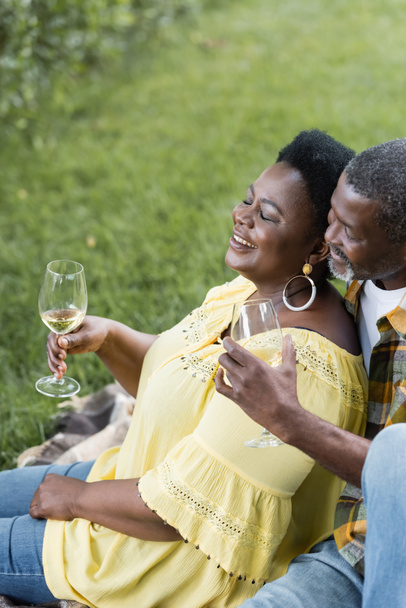 vysoký úhel pohledu na usmívající se a starší africký pár drží sklenice vína - Fotografie, Obrázek