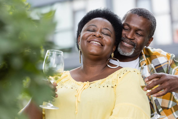 radostný a starší africký pár drží sklenice vína - Fotografie, Obrázek