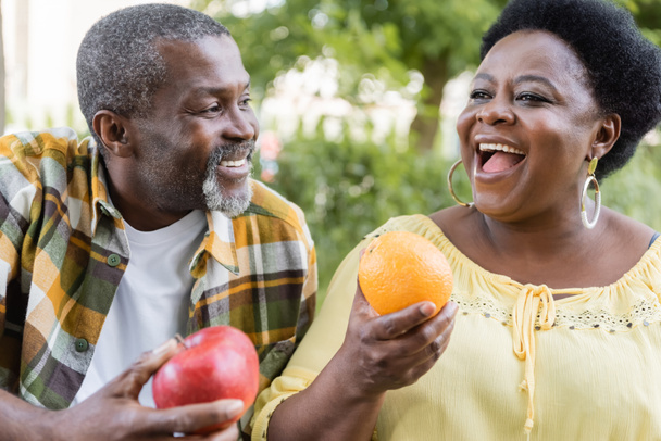 allegra e anziana coppia afro-americana che tiene frutta durante il picnic  - Foto, immagini