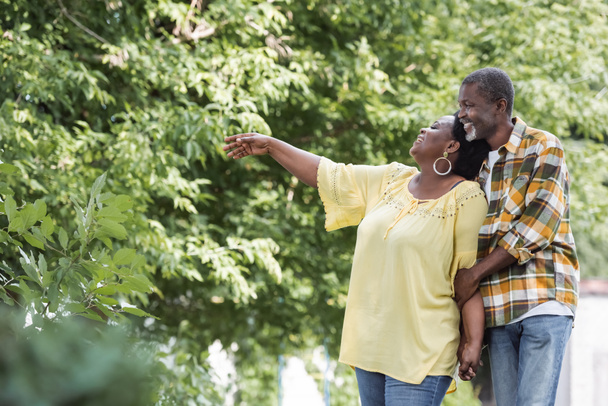 felice donna afroamericana anziana indicando con mano vicino al marito nel parco  - Foto, immagini