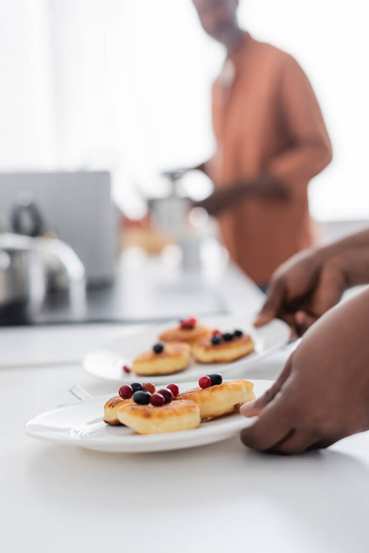 обрезанный вид на африканскую американку, держащую тарелки с украинскими блинами и ягодами - Фото, изображение