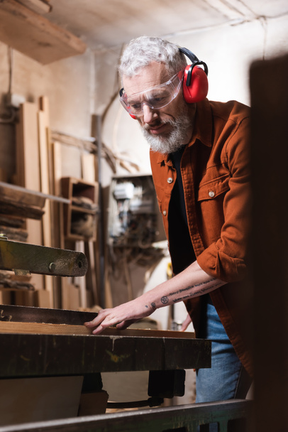 bearded carpenter working at workbench on blurred foreground - Photo, Image