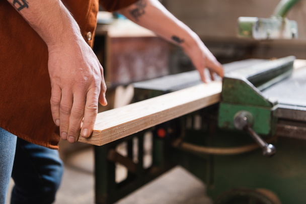 Teilansicht tätowierter Möbeldesigner mit Holzplanke im Holzwerkatelier - Foto, Bild