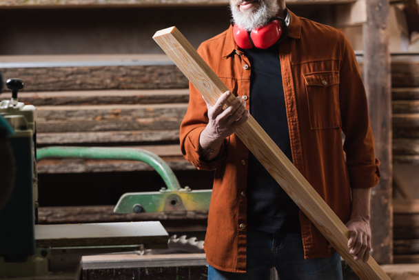 обрезанный вид бородатого дизайнера мебели держа деревянную доску в мастерской - Фото, изображение