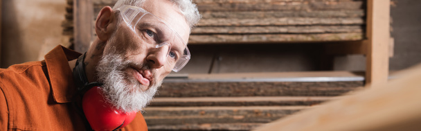 bearded furniture designer in goggles working in woodwork studio, banner - Photo, Image