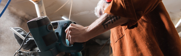 low angle view of tattooed carpenter working with miter saw in workshop, banner - Photo, Image
