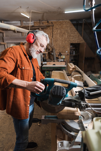 bearded woodworker cutting board with miter saw in workshop - Photo, Image