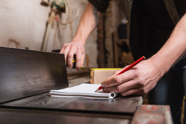 Ausgeschnittene Ansicht eines Tischlers, der während seiner Arbeit in der Werkstatt in Notizbuch schreibt - Foto, Bild