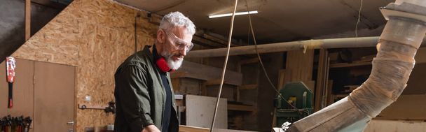 carpintero de mediana edad en gafas de trabajo en estudio de carpintería, pancarta - Foto, Imagen