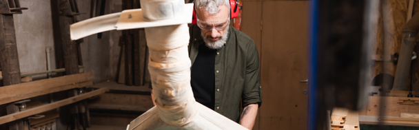 bearded carpenter in goggles working near blurred ventilation hood, banner - 写真・画像