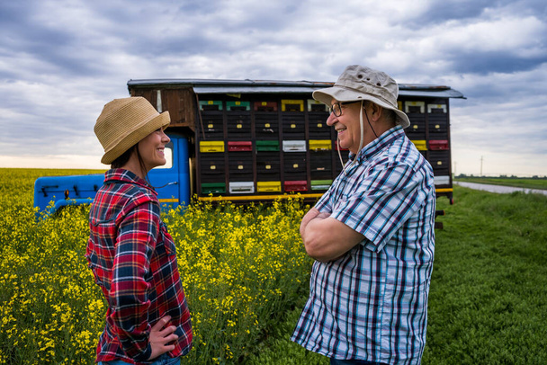Twee generaties bijenhouders staan voor hun truck met bijenkorven. Senior man leert zijn opvolger over de bijenteelt. - Foto, afbeelding