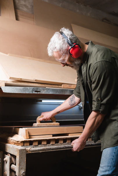 side view of grey haired carpenter polishing board in sander machine - Photo, Image