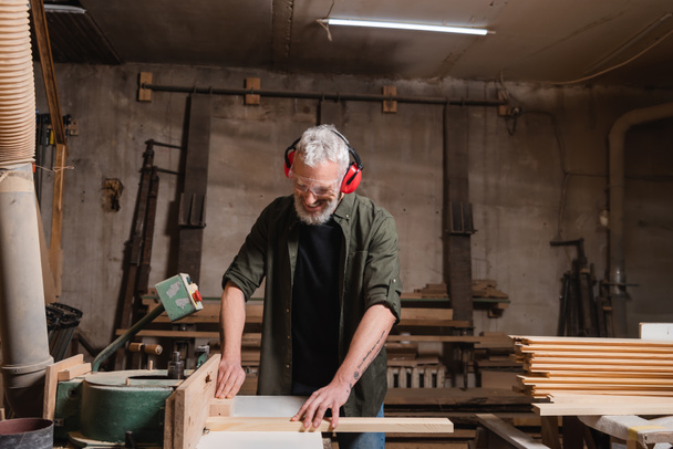 carpintero de mediana edad feliz trabajando en la máquina de unión en el taller - Foto, Imagen