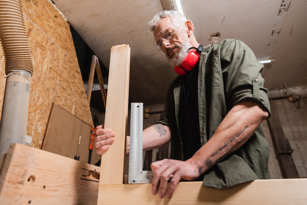 Vista de bajo ángulo del diseñador de muebles midiendo detalles de madera en estudio de carpintería - Foto, Imagen