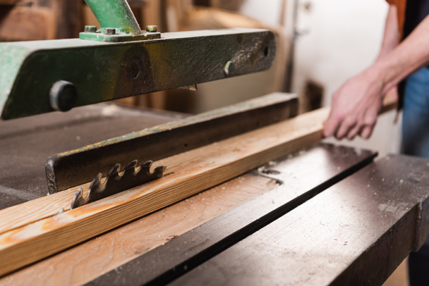 partial view of woodworker cutting plank on circular saw in carpentry workshop - Φωτογραφία, εικόνα