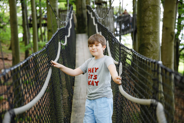 Preteen kid boy walking on high tree-canopy trail with wooden walkway and ropeways on Hoherodskopf in Germany. Happy active young child exploring treetop path. Funny activity for families outdoors - Photo, Image