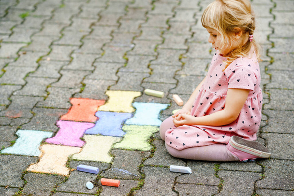 Маленька дівчинка дошкільного віку малює різнокольоровими чашами на землі на задньому дворі. Позитивний щасливий малюк малюк малює і створює картини. Творча активність на відкритому повітрі влітку
. - Фото, зображення