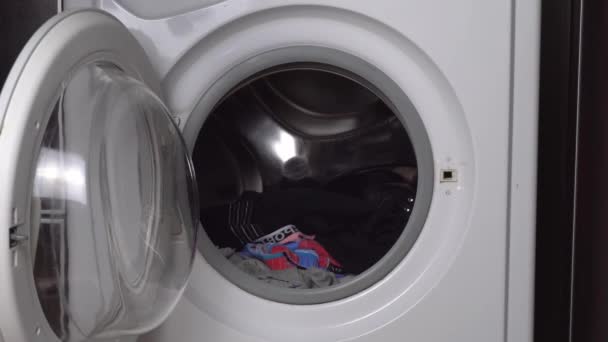 Женские руки грузят одежду, нижнее белье и предметы гардероба в стиральную машину - Кадры, видео