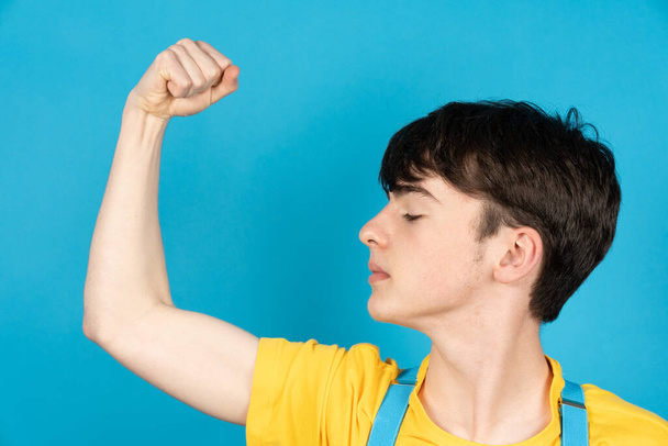 Delgado adolescente orgulloso mirando a su músculo bíceps. Bandera de Ucrania colores - Foto, imagen