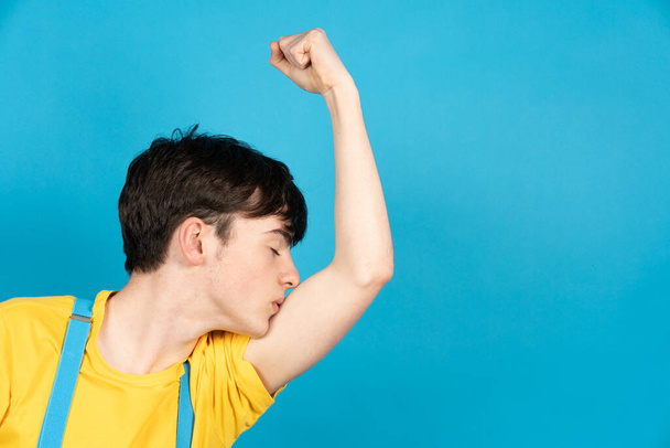 Dumny nastolatek chłopiec całuje jego bicepsy izolowane na niebieskim tle - Zdjęcie, obraz
