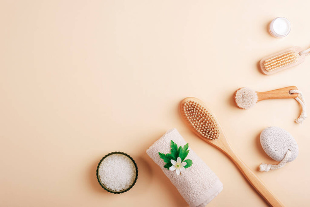 Natural bath accessories and cosmetics. Face and body brushes, sea salt, towel, pumice stone and cream in jar on light neutral background. Top view, copy space. - Photo, Image