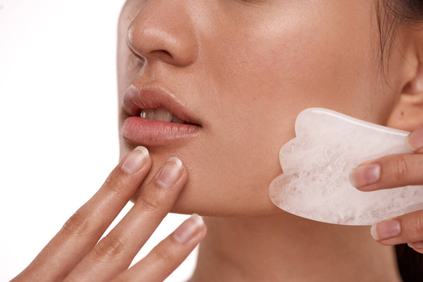 For smoother, firmer skin. Shot of a beautiful woman using a Gua Sha tool on her face. - 写真・画像