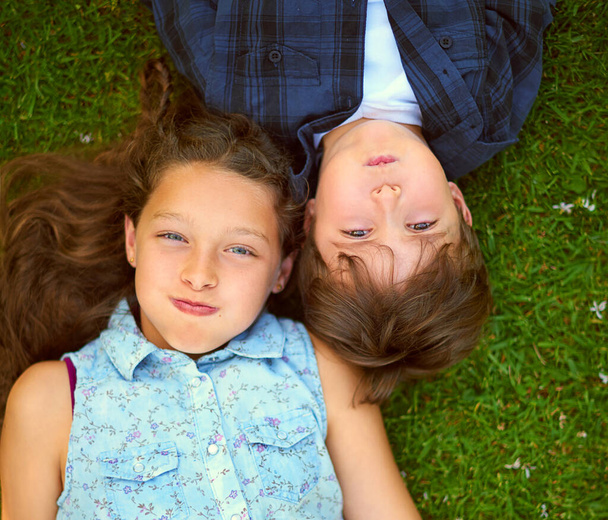 Haltet den Atem an. Hochwinkelaufnahme eines jungen Geschwisterpaares, das den Atem anhält, während es draußen im Gras liegt. - Foto, Bild