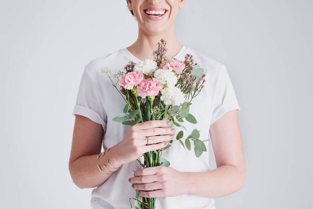 Glück kommt von Blumen. Studioaufnahme einer unkenntlichen Frau mit einem Blumenstrauß vor grauem Hintergrund. - Foto, Bild
